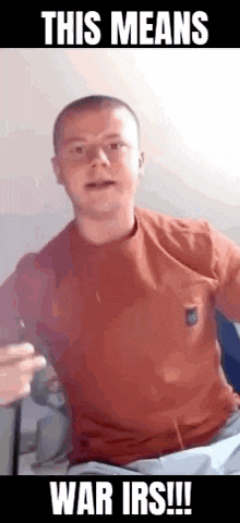 a man in a red shirt is sitting on a bed and talking to a camera .