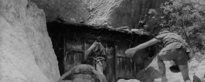 a black and white photo of two people standing next to each other in front of a building .