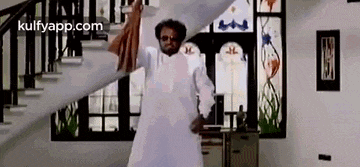 a man in a white dress is standing in front of a staircase in a room .