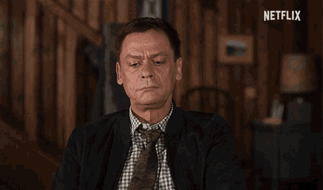 a man in a suit and tie is sitting in front of a netflix sign
