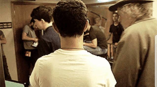 a man in a white shirt is standing in front of a group of people in a room .