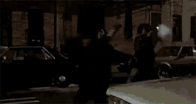 a man is holding a flashlight while standing next to a car in a dark street .