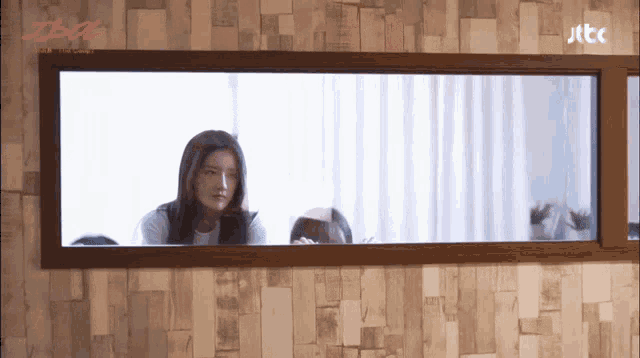 a woman looking out a window with jtcc written on the bottom right