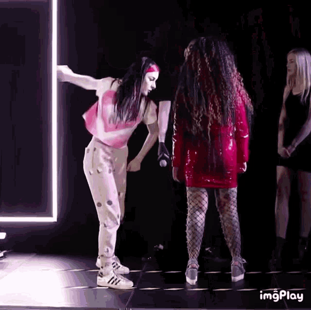 a woman in a red dress is standing next to another woman in a pink top