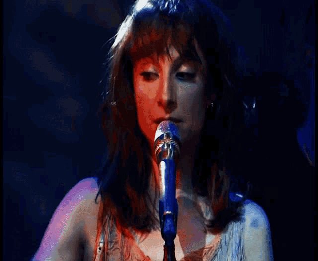 a woman singing into a blue microphone with a smile on her face