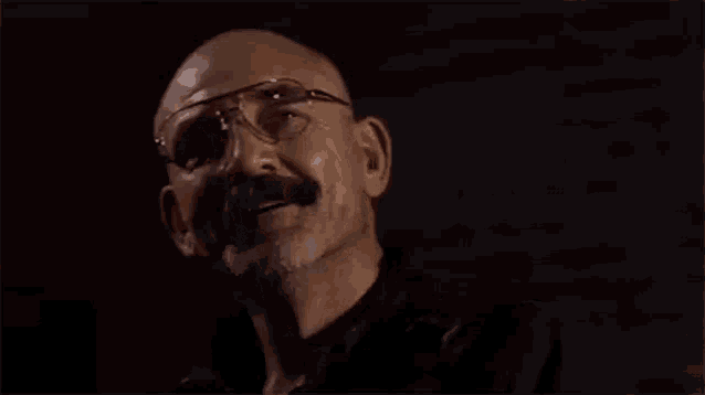 a bald man wearing glasses and a mustache is laughing .