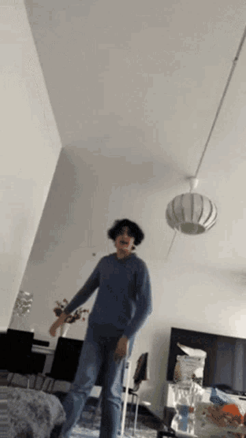 a man is dancing in a living room with a lamp hanging from the ceiling .