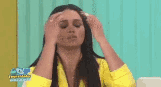 a woman in a yellow jacket is holding her head in pain .