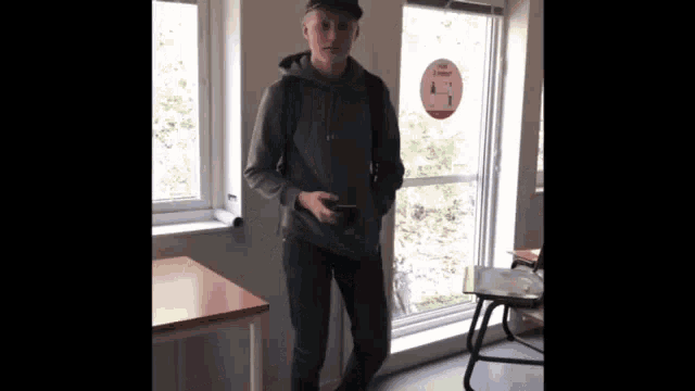 a young man standing in front of a window holding a cell phone