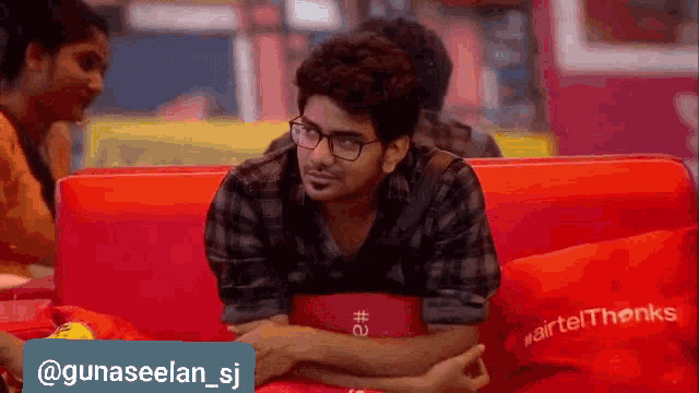 a man wearing glasses is sitting on a red couch with red pillows .