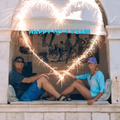 a man and a woman are sitting on a window sill with sparklers in the shape of a heart and the words happy new year