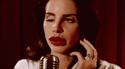 a woman is singing into a microphone with red lipstick and a green ring .