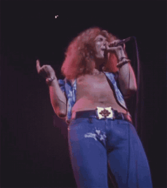 a shirtless man singing into a microphone with a belt that has a x on it