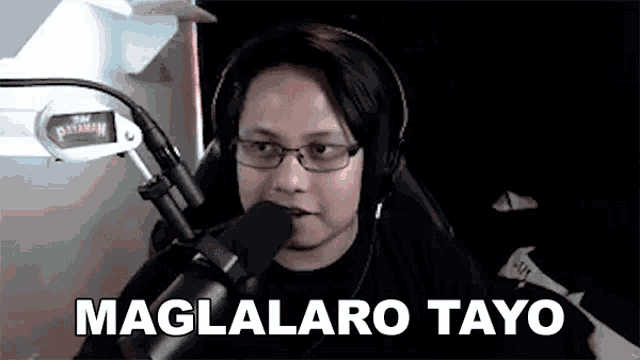 a man wearing headphones and glasses is sitting in front of a microphone and saying maglalaro tayo .