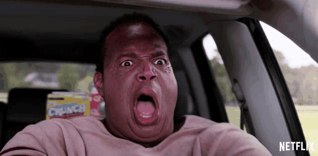a man sitting in a car with his mouth open and a box of crunch cereal in the background