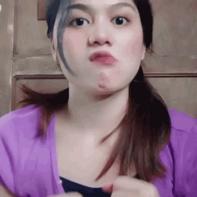 a woman in a purple shirt is making a funny face while holding her hair in a ponytail .