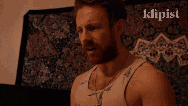 a man with a beard says you ungrateful bitch in front of a tapestry