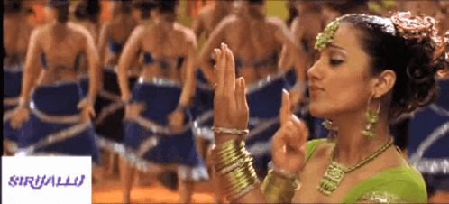 a woman in a green top is dancing in front of a sign that says siruallu