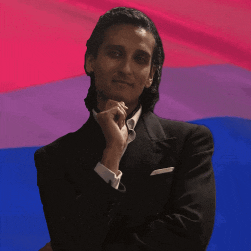 a man in a suit is standing in front of a pink and blue flag
