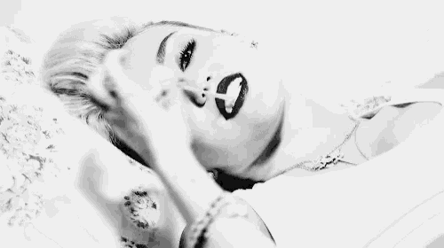 a black and white photo of a woman laying on a bed with a cigarette in her mouth .