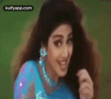 a woman with long hair is wearing a blue saree and earrings and is smiling .