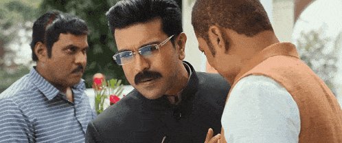 a man with glasses and a mustache talks to a man in a white shirt