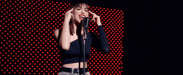 a woman singing into a microphone with a red background