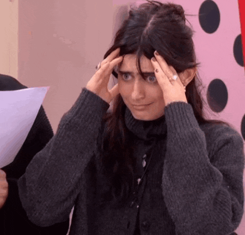a woman in a grey sweater is holding her head in pain