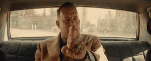 a man in a suit and tie is sitting in the back seat of a car and pointing at something .