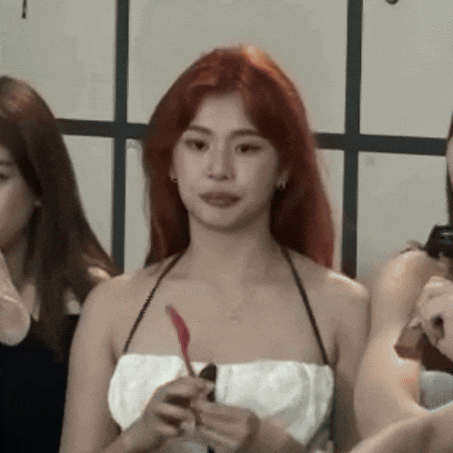 a woman with red hair is wearing a white top and holding a red pen .