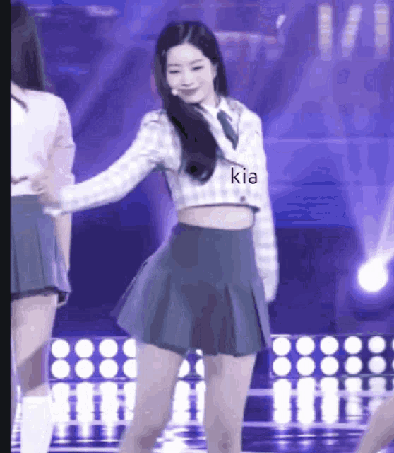 a woman in a crop top and pleated skirt is dancing on a stage with kia written on her shirt