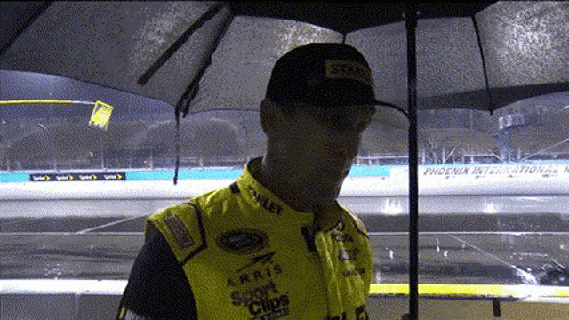 a man stands under an umbrella with a phoenix international race track behind him