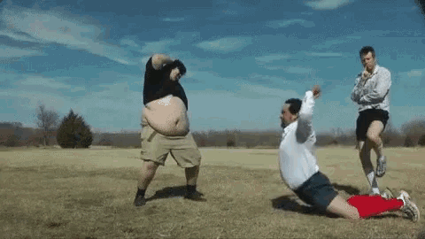a group of men are dancing in a field and one of them has a huge belly