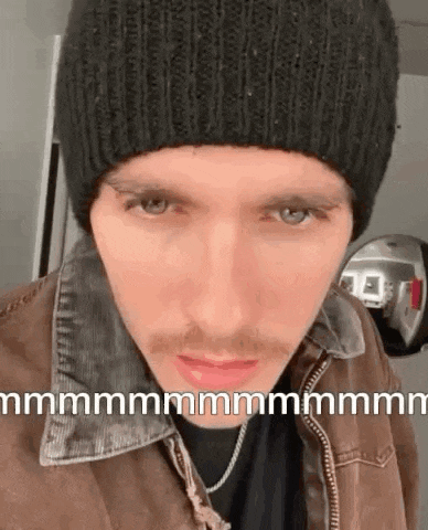 a man wearing a black beanie and a brown jacket is making a funny face .