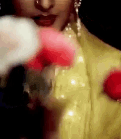 a woman in a yellow dress is wearing boxing gloves and holding a red flower .