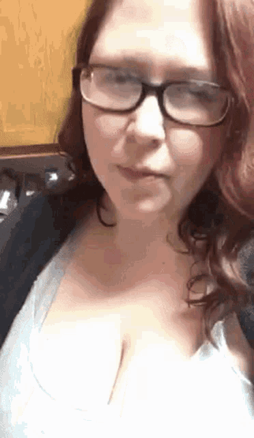 a woman wearing glasses and a white shirt is looking at the camera .