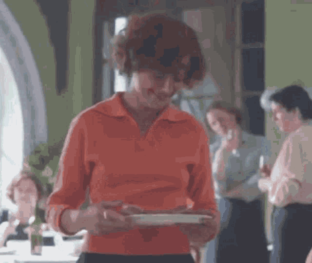 a woman in an orange shirt is holding a plate of food in a restaurant .