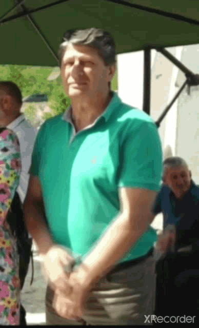 a man in a green shirt is standing under an umbrella