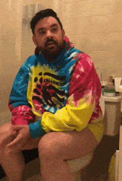 a man is sitting on a toilet wearing a colorful tie dye shirt that says calimar
