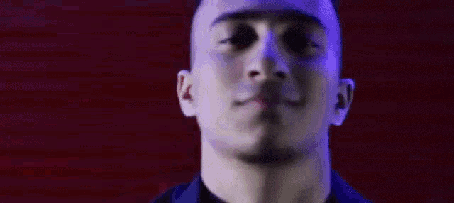a close up of a man 's face with a red background and a purple light behind him .