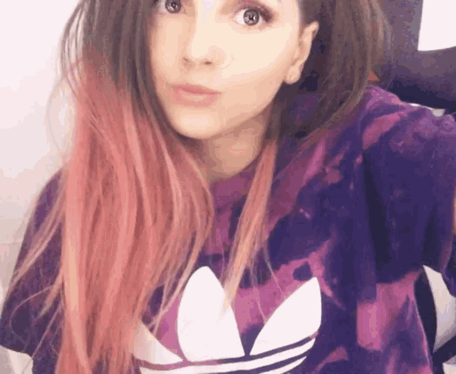a woman with pink hair is taking a selfie in a purple adidas shirt .