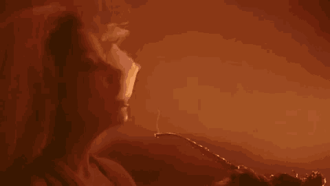 a woman is smoking a hookah in a dark room and smoke is coming out of her mouth .