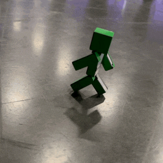 a green toy is walking on a gray floor