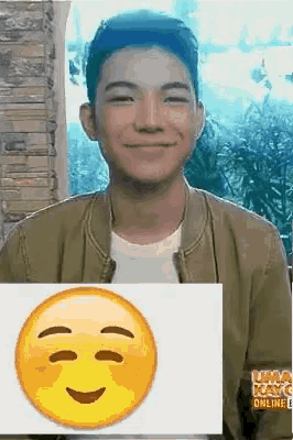 a young man is smiling and holding a picture of a smiley face