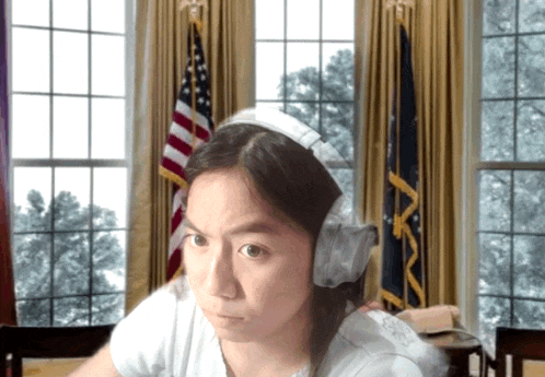 a woman wearing headphones is sitting in front of a window with an american flag in the background