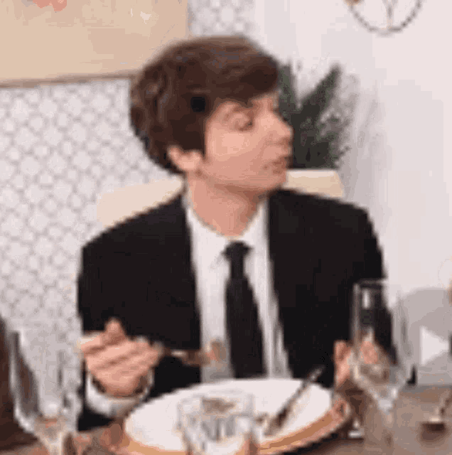 a man in a suit and tie is sitting at a table eating with a fork and knife .