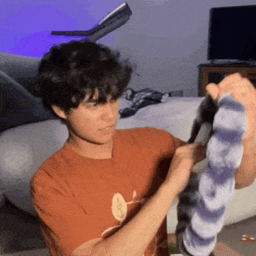 a young man in an orange shirt is holding a tie dye shirt in his hands