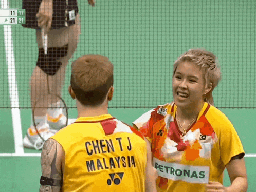 a man and a woman are playing badminton and the man is wearing a yellow jersey that says chen tj malaysia