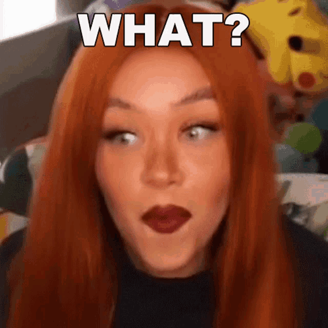 a woman with red hair is making a funny face with the words what written on her face .