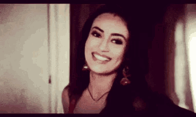 a woman wearing earrings and a necklace is smiling for the camera